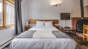 Un dormitorio con una cama grande, televisión, chimenea y una ventana con cortinas.
