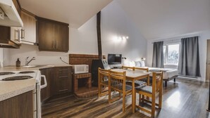 Cocina compacta con estufa, microondas y lavamanos. Hay un comedor con mesa y sillas, y una cama con ventana.