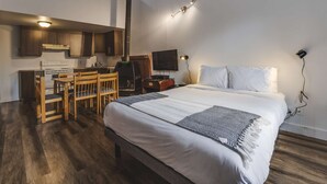 Una habitación de hotel compacta con cama, una kitchenette pequeña, zona de comedor y televisión.