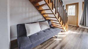 Un sofá gris con cojines blancos en una habitación con suelo de madera y una escalera de madera.