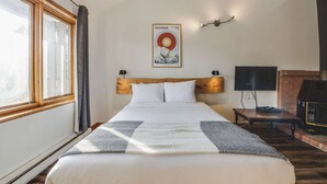 Una habitación de hotel con una cama grande, televisor montado, chimenea y una ventana con cortinas.
