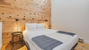 A bedroom with a wooden slat ceiling, a bed with white bedding, a black and white throw blanket, and a small round table with a lamp. - Studio Courchevel 3 (Mezz 2 Q - 1 DL) - 6 people (Saint-Ferréol-les-Neiges)