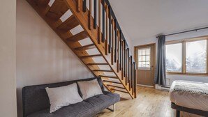 A modern loft bedroom with a wooden staircase, a gray sofa, a bed, and a large window. - Studio Courchevel 3 (Mezz 2 Q - 1 DL) - 6 people (Saint-Ferréol-les-Neiges)