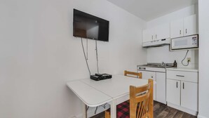A compact kitchen with a white table and chairs, a flat-screen TV mounted above the table, and a microwave above the stove. - Studio St-Anton 4 (1 Q) - 2 people (Saint-Ferréol-les-Neiges)
