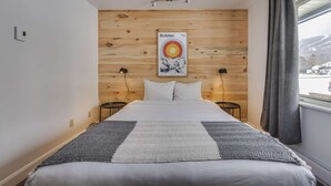 A bedroom with a wooden headboard, a bed with white bedding, two bedside lamps, and a poster on the wall. - Studio St-Anton 4 (1 Q) - 2 people (Saint-Ferréol-les-Neiges)