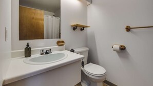 Et badeværelse med en hvid vask, et toilet, et spejl og en træhylde.