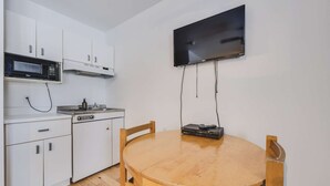 A compact kitchen with white cabinets, a microwave, a stove, and a TV mounted on the wall. - Studio St-Anton 8 (1 Q) - 2 people (Saint-Ferréol-les-Neiges)