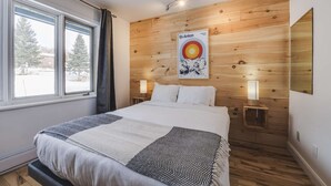 A bedroom with a bed, two bedside lamps, a poster on the wall, and a window with curtains. - Studio St-Anton 8 (1 Q) - 2 people (Saint-Ferréol-les-Neiges)
