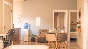 A modern hotel room with a dining area, a water dispenser, a potted plant, and a bed.