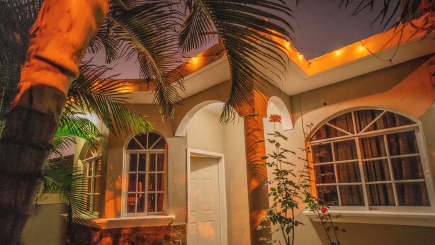 A building with arched windows and a door, surrounded by palm trees and a stone wall.