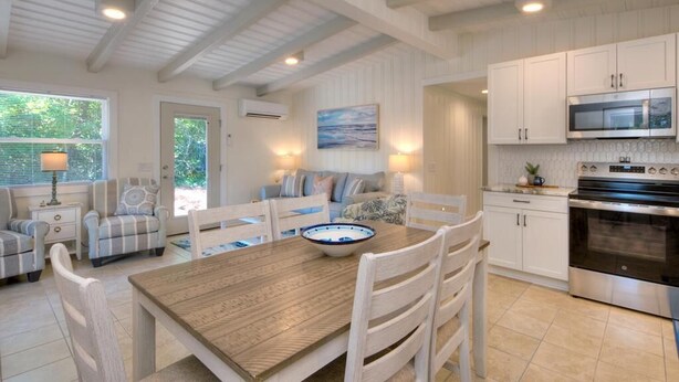 A spacious kitchen with white cabinetry, a large stove, and a dining area with a wooden table and white chairs. - Experience coastal bliss at Sand Dollar Daze, a spacious 3-bedroom home in Oak Island. (Oak Island)