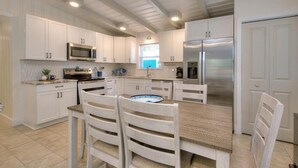 A modern kitchen with white cabinetry, stainless steel appliances, and a wooden dining table with chairs. - Experience coastal bliss at Sand Dollar Daze, a spacious 3-bedroom home in Oak Island. (Oak Island)