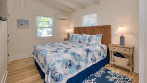A bedroom with a bed, two bedside lamps, a window, and a wall-mounted air conditioner. - Experience coastal bliss at Sand Dollar Daze, a spacious 3-bedroom home in Oak Island. (Oak Island)