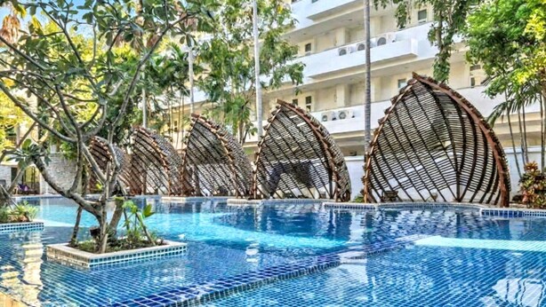A swimming pool with clear blue water, surrounded by a tiled deck and palm trees.