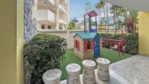 A children's play area with a small playhouse, a swing set, and decorative stone planters.