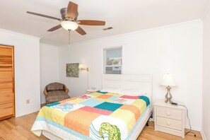 A bedroom with a bed, a chair, a nightstand, a lamp, a ceiling fan, and a window with blinds. - Fancy Free - Oceanfront 4 BR. (Surf City)