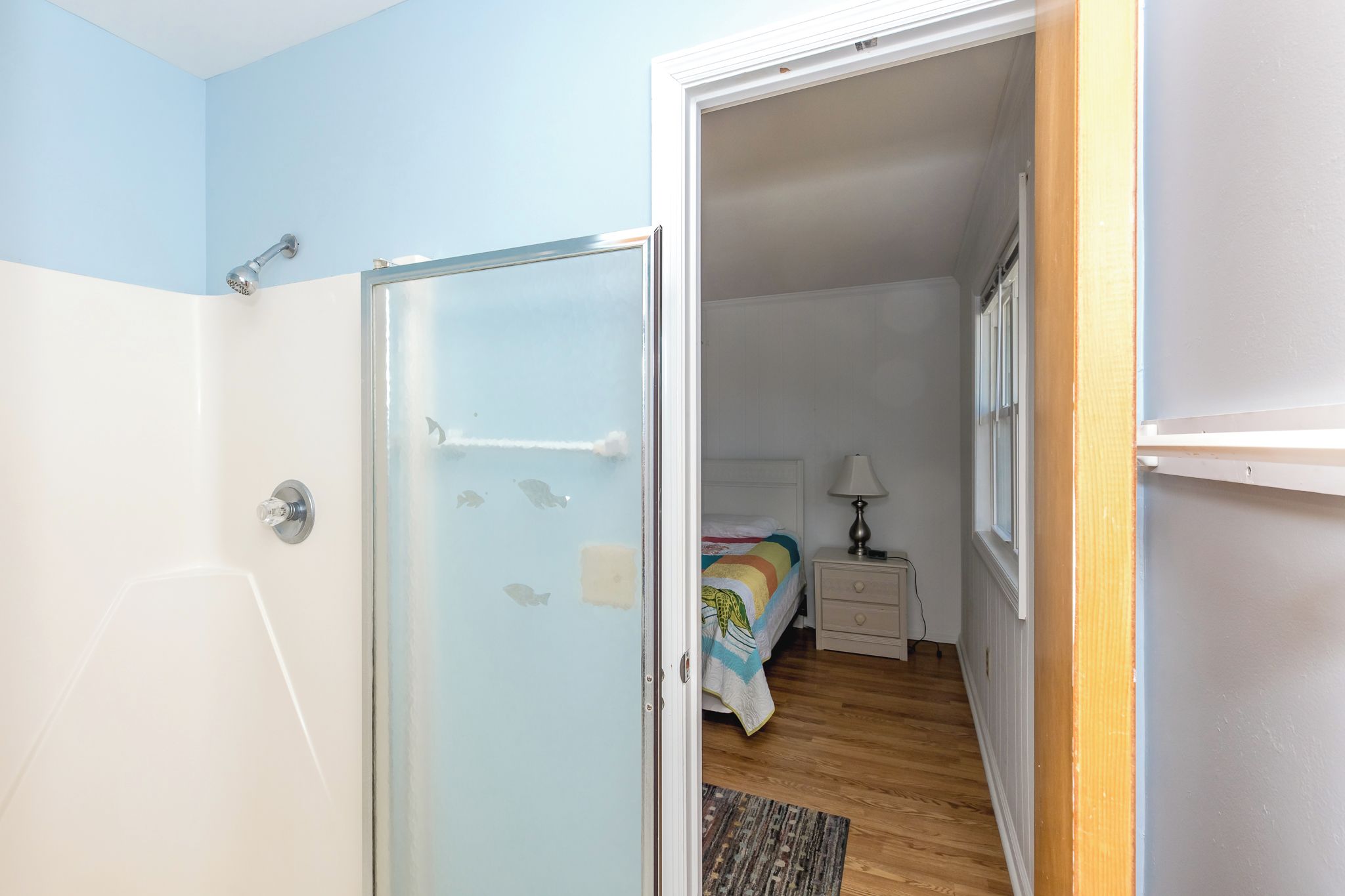A room with a bed, bedside table, lamp, and a door leading to another room.
