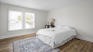 A bedroom with a large bed, a nightstand, a lamp, and a window with blinds.