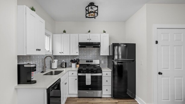 A modern kitchen with white cabinets, stainless steel appliances, and a wooden floor.