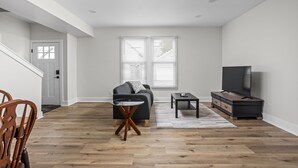 A modern living room with a sofa, coffee table, TV stand, and a dining area with chairs.