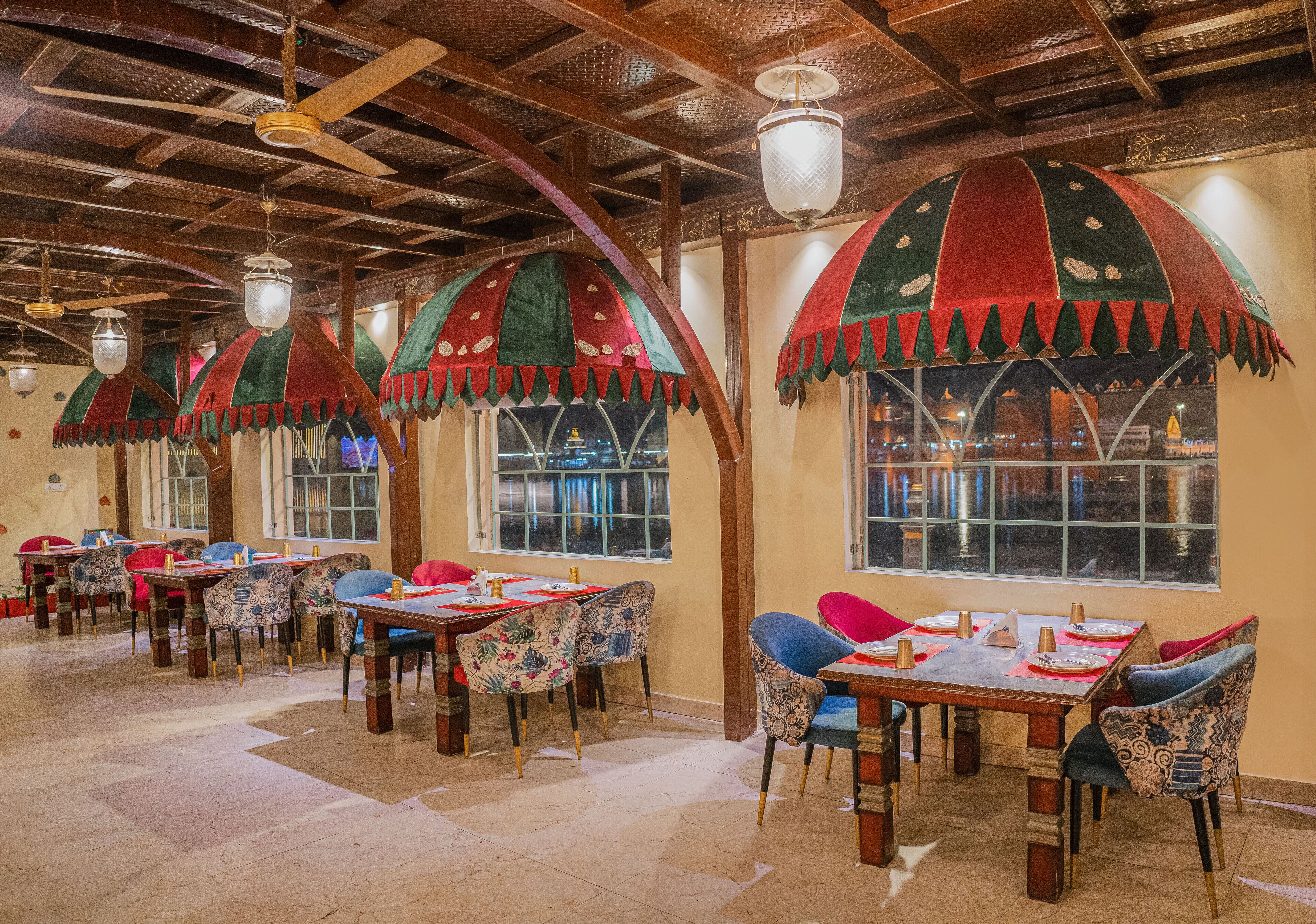 Un restaurante con mesas y sillas de madera, sombrillas decorativas y amplios ventanales.
