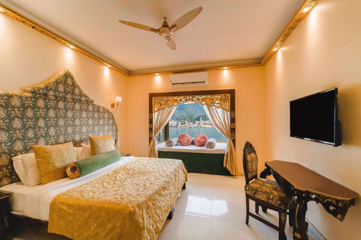 A hotel room with a large bed, a desk, a chair, a TV, and a window with curtains.