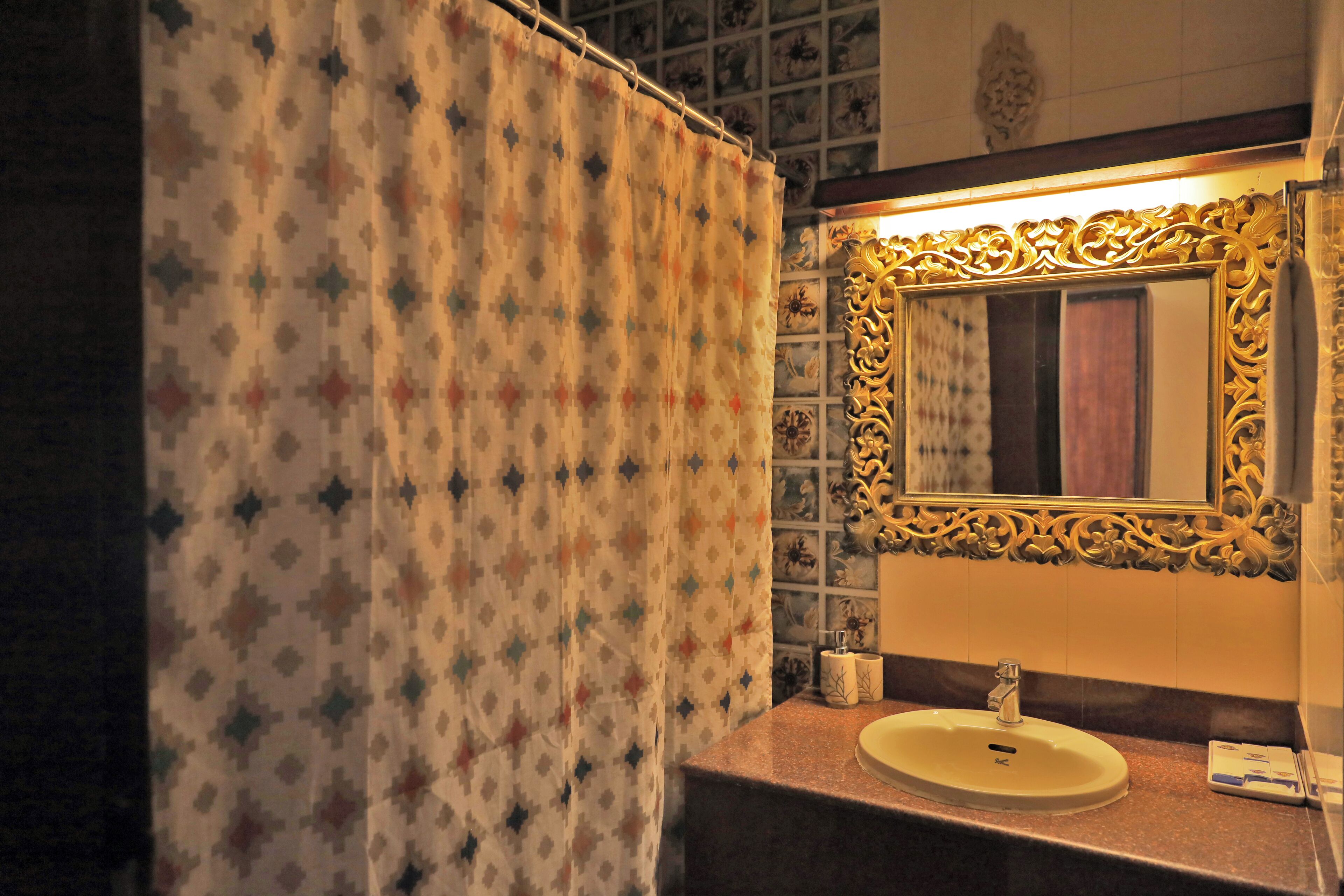 A bathroom with a patterned shower curtain, a sink with a gold-framed mirror, and a tiled wall with a decorative border.
