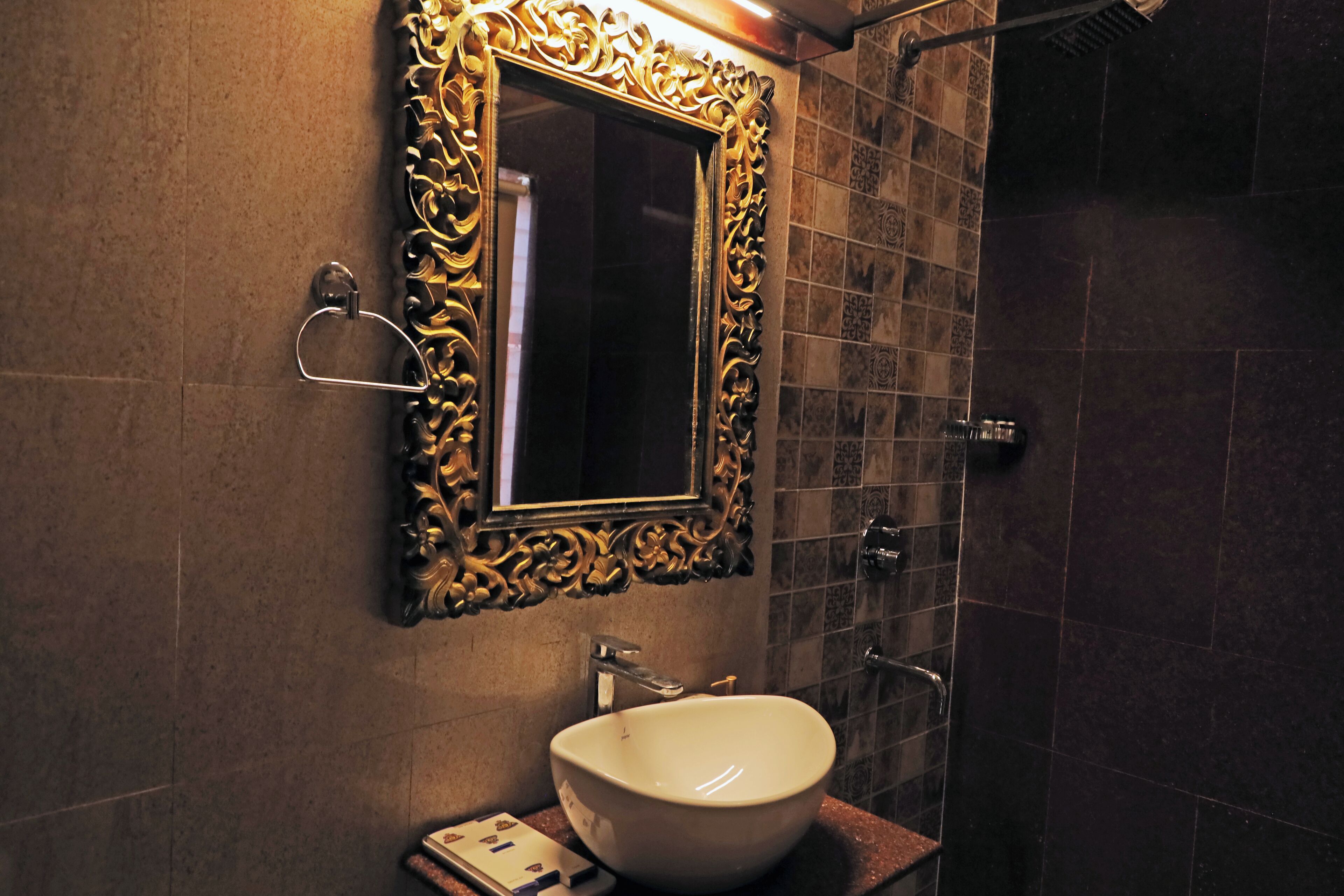 Un baño con un espejo grande y decorativo, un lavabo blanco y una zona de ducha.