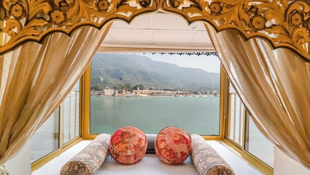 Ein Zimmer mit einem Bett, zwei Zierkissen und Blick auf einen See und Berge durch ein Fenster mit Vorhängen.