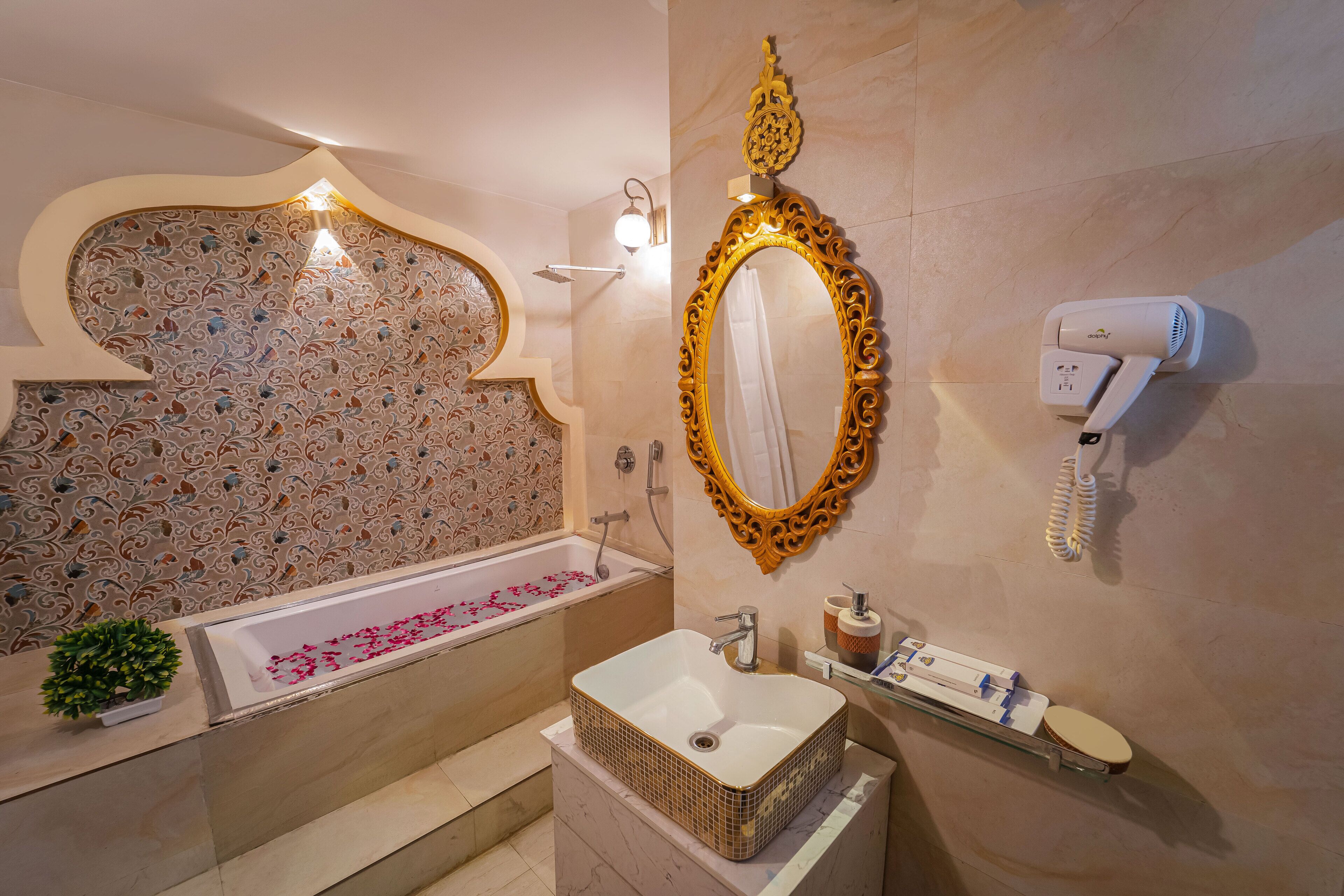 Un baño con bañera, lavamanos, espejo, secador de pelo y decoración en la pared.