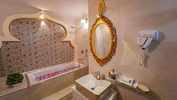 Un baño con bañera, lavamanos, espejo, secador de pelo y decoración en la pared.