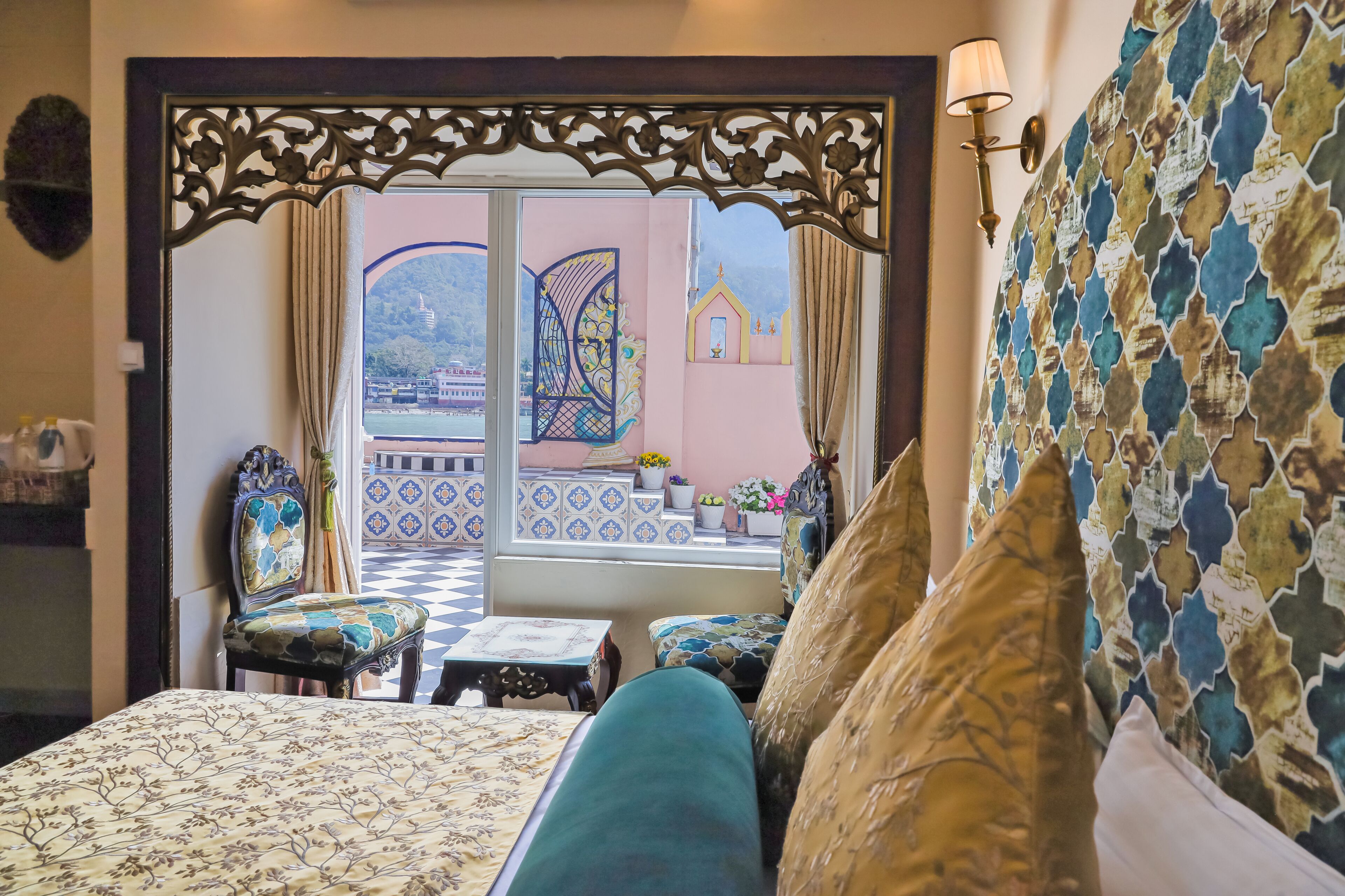 Una habitación con una cama, una mesita y una silla. Hay una ventana con vista a un balcón y un edificio.