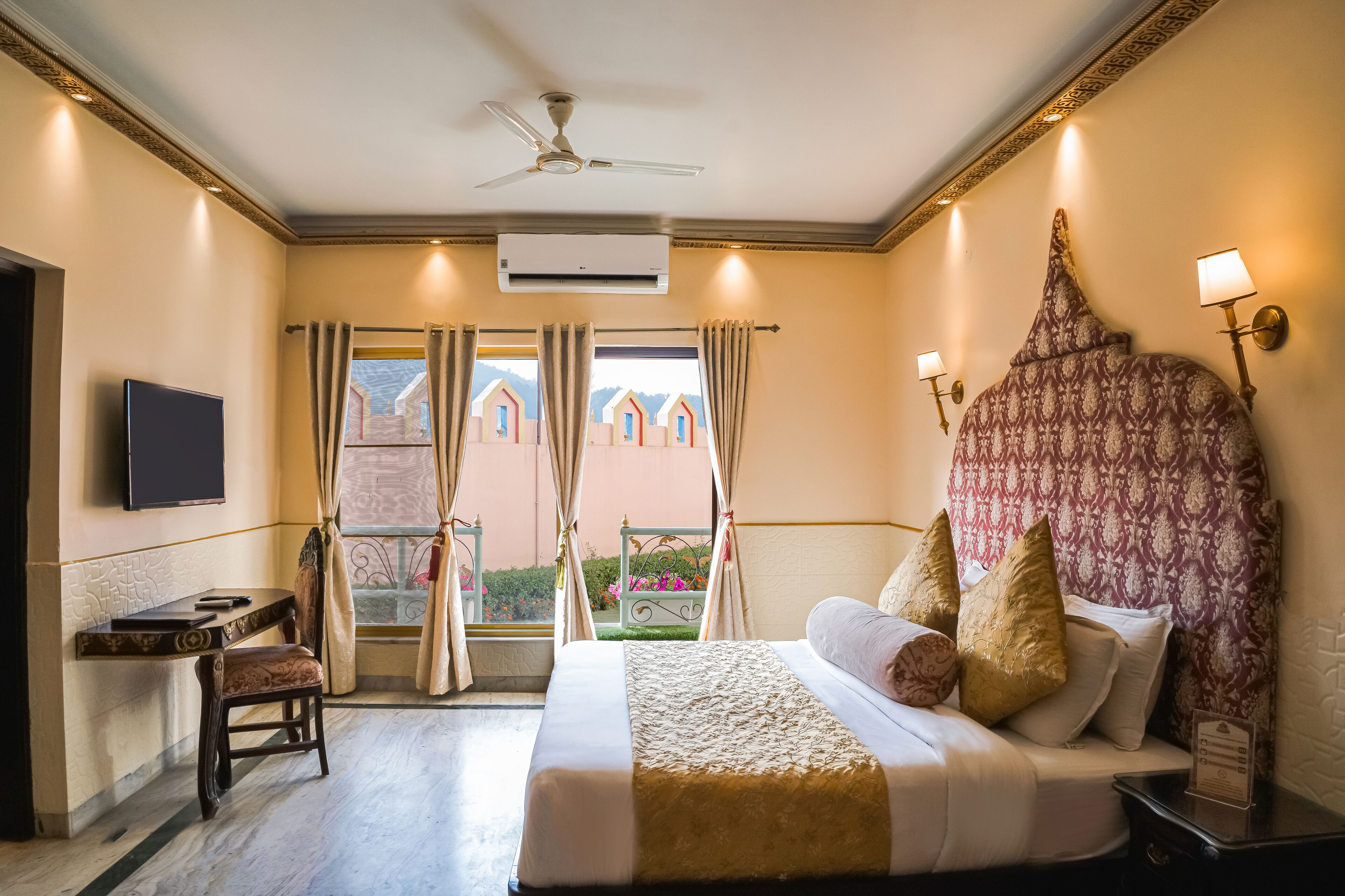 A hotel room with a bed, a desk, a chair, a TV, and a balcony with curtains.