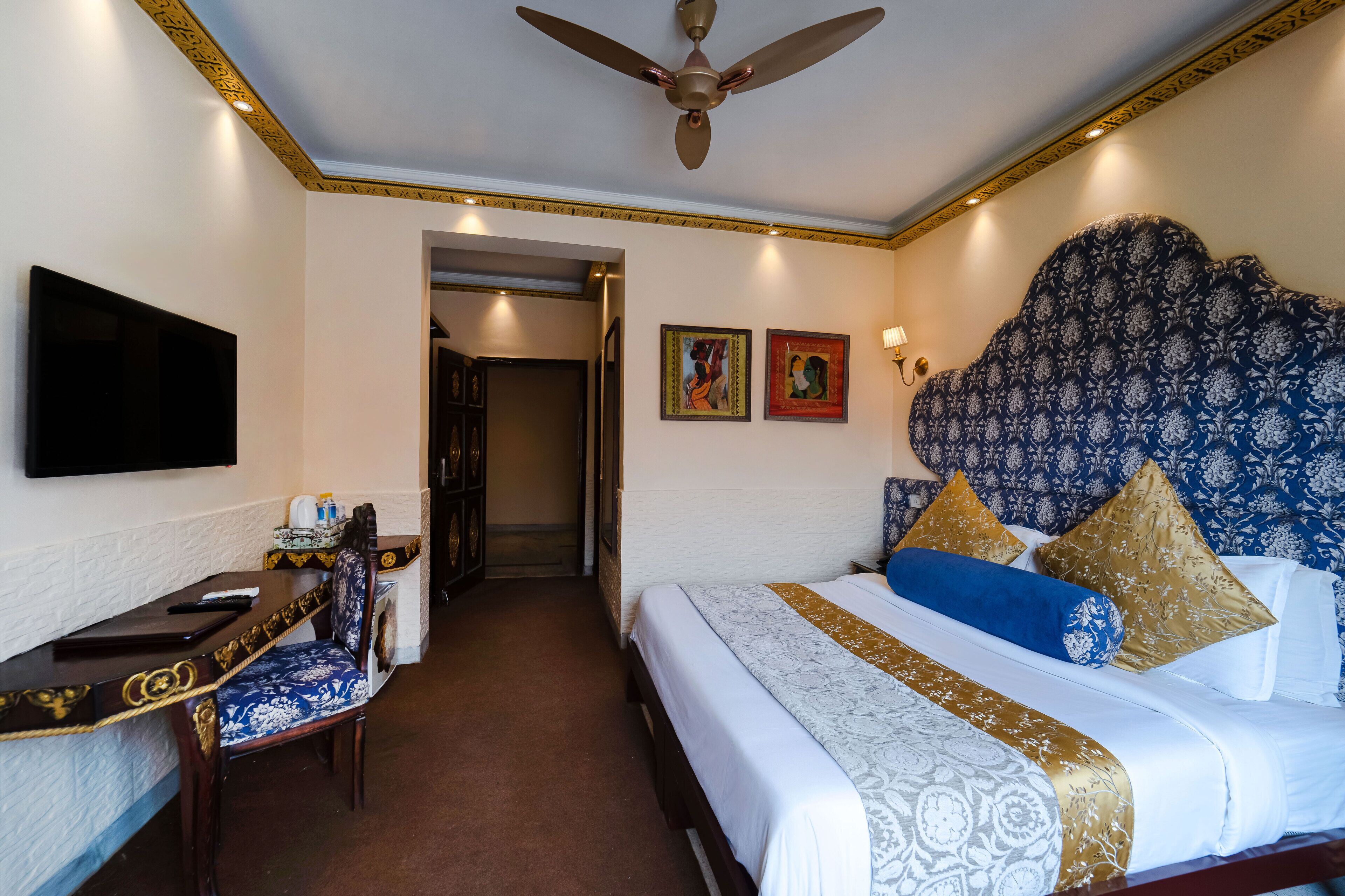 Une chambre d’hôtel équipée d’un lit, d’un bureau, d’une chaise, d’une télévision et d’un ventilateur de plafond.