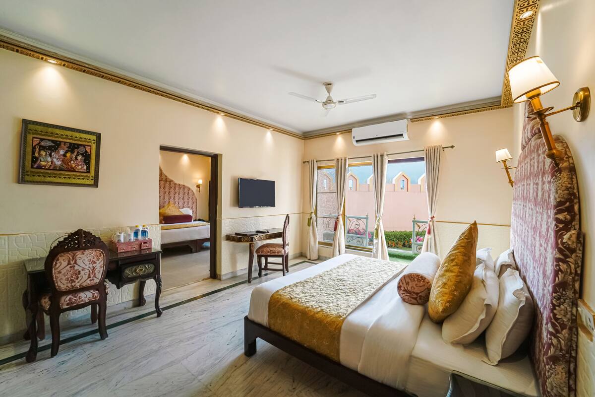 A hotel room with a bed, desk, chair, television, and a balcony with curtains.