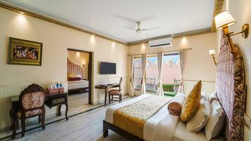 Quarto de hotel com cama, escrivaninha, cadeira, televisão e varanda com cortinas.