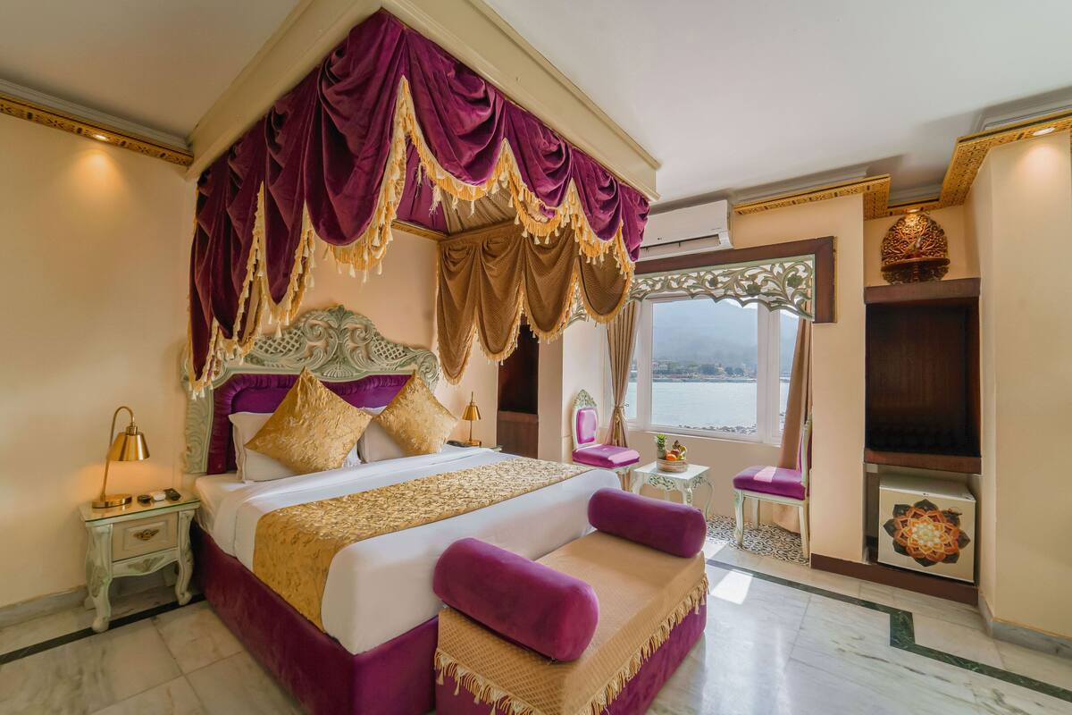A large bed with a canopy, a nightstand, a chair, and a view of the outdoors.