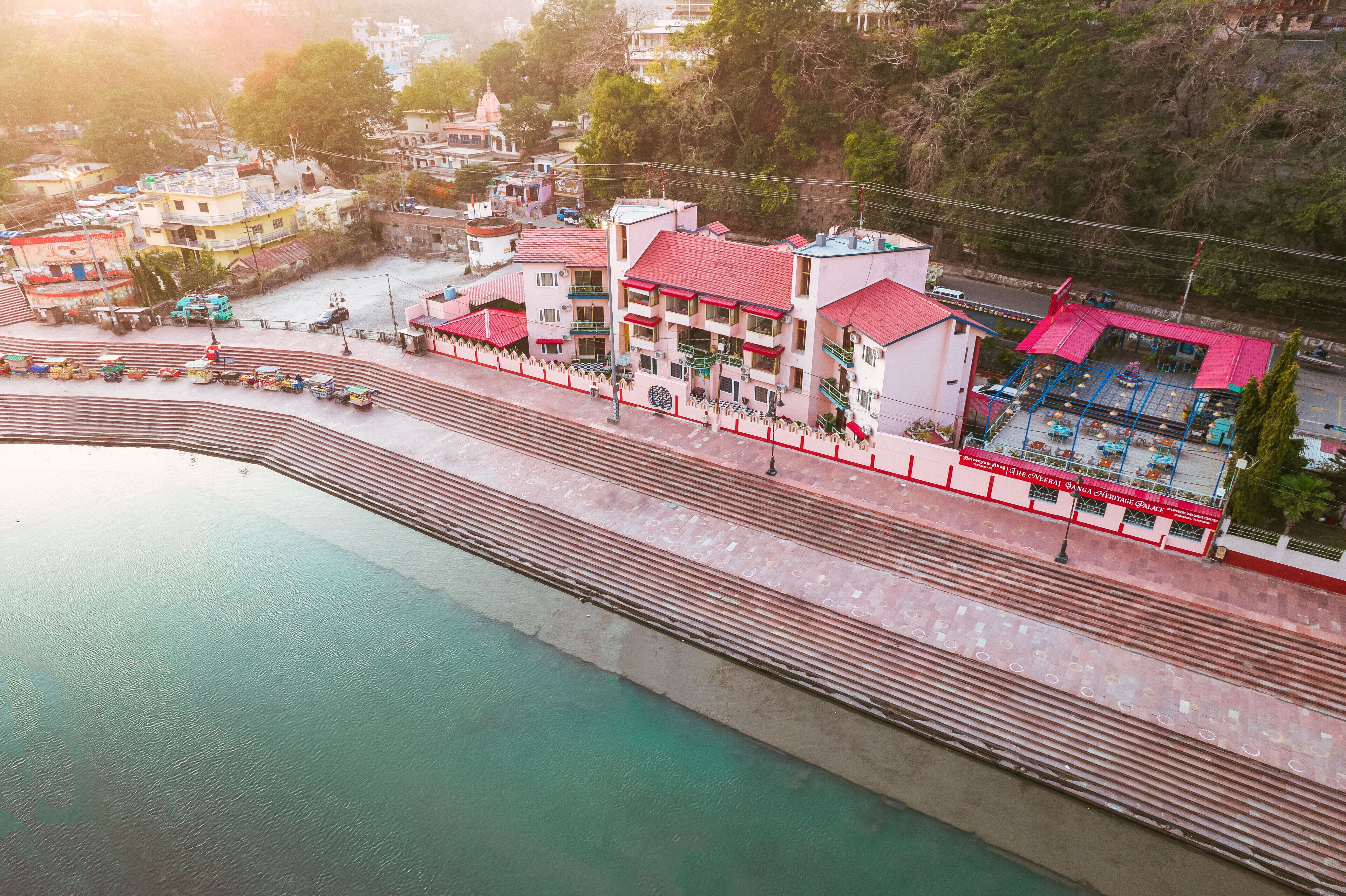 A riverside hotel with a red-roofed building, a swimming pool, and a view of the river.