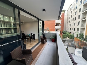 A balcony with a dining area, potted plants, and a view of adjacent buildings. - Sydney"Modern 2-Bedroom Apartment near Airport & Beach – Rockdale train  NSW (Rockdale)