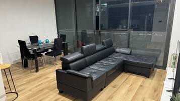 A modern living room with a sectional sofa, a dining table with chairs, and a large window with a view.