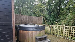 A hot tub on a wooden deck with a wooden fence and trees in the background. - Glan yr Afon Un - Relax, Recuperate, Enjoy (Welshpool)