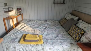 A bedroom with a bed, pillows, a bedside table, and a shelf with books. - Glan yr Afon Un - Relax, Recuperate, Enjoy (Welshpool)