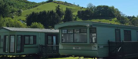 A row of green mobile homes with a grassy hill in the background.