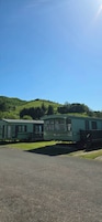 A row of green mobile homes with a grassy hill in the background.