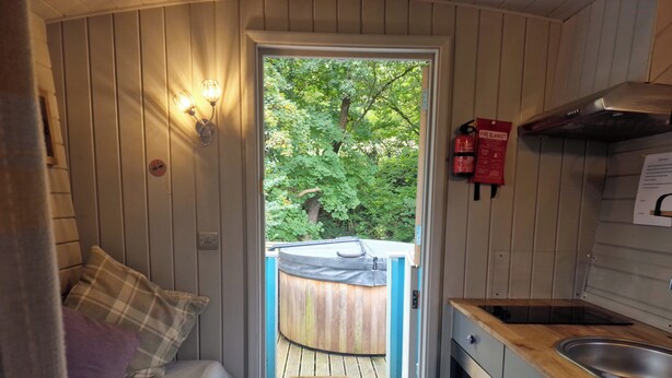 A compact room with a bed, a small kitchenette, and a door leading to an outdoor deck. - Glan yr Afon Dau - Relax, Recuperate, Hot Tub (Welshpool)