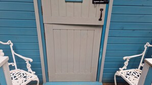 A door with a small window and a lock, flanked by two white chairs with intricate designs. - Glan yr Afon Dau - Relax, Recuperate, Hot Tub (Welshpool)