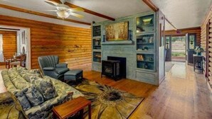 A log cabin interior with a sofa, armchair, fireplace, and wooden shelves. - Quarter Horse Inn - Heather Room | Historic Inn | Fireplace | Walk to Downtown & Rail Station (Flagstaff)