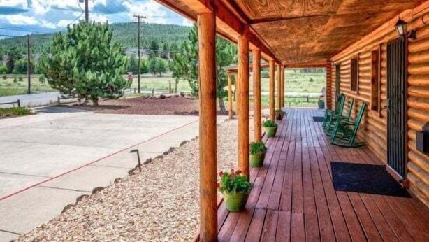 A wooden cabin with a covered porch, outdoor seating, and a view of a mountainous landscape. - Quarter Horse Inn - OrchidRoom | Historic Log Inn | Fireplace | Walk to Downtown & Rail Station (Flagstaff)