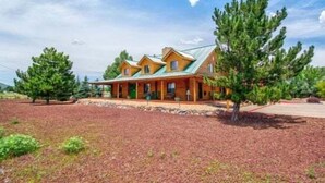 A log cabin with a green roof, surrounded by a red mulch ground cover and several pine trees. - Quarter Horse Inn - OrchidRoom | Historic Log Inn | Fireplace | Walk to Downtown & Rail Station (Flagstaff)