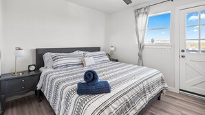 A bedroom with a bed, a nightstand, a ceiling fan, a window with curtains, and a view of the outdoors. - The Heritage Hideaway Views Games & More (Leander)
